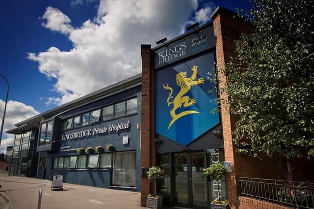 Exterior view of Kingsbridge Private Hospital building with a large blue and gold sign featuring a griffin emblem, under a partly cloudy sky.