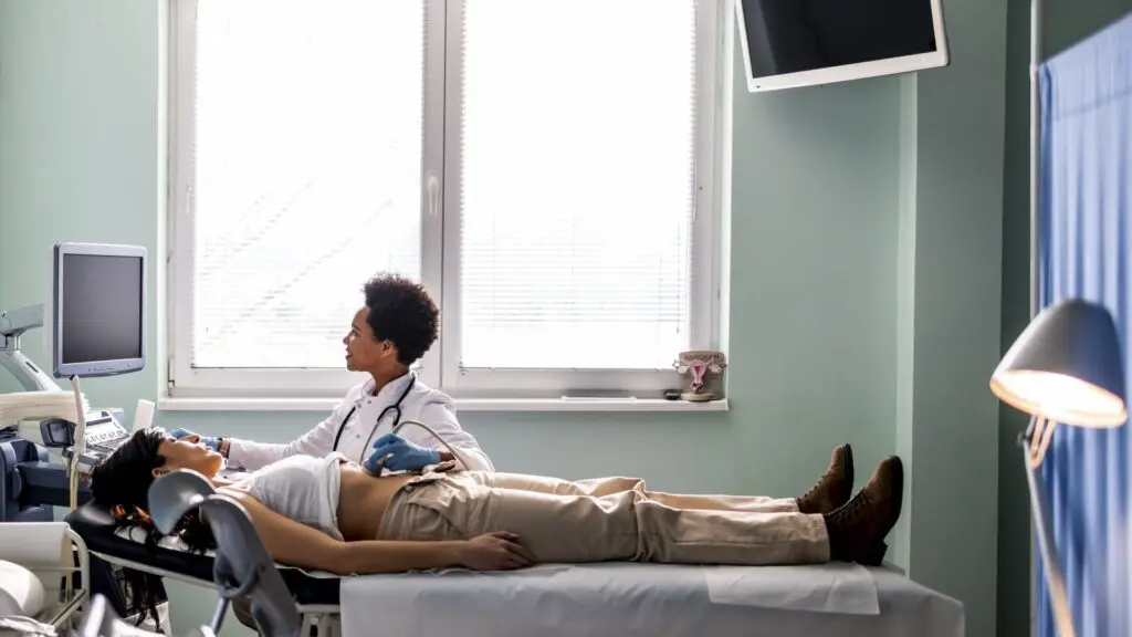 A doctor performs an ultrasound scan on a patient lying on an examination couch in a medical surgery.