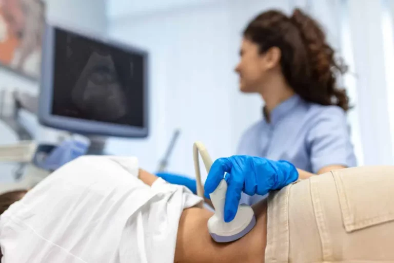 A healthcare professional performs an abdominal ultrasound on a patient using a handheld device, with the ultrasound image displayed on a monitor.