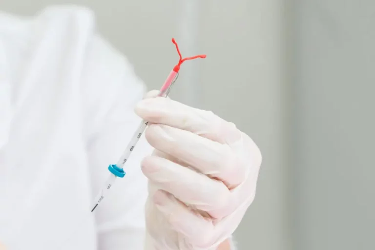 A gloved hand holds an intrauterine device (IUD) with an applicator, prepared for insertion.