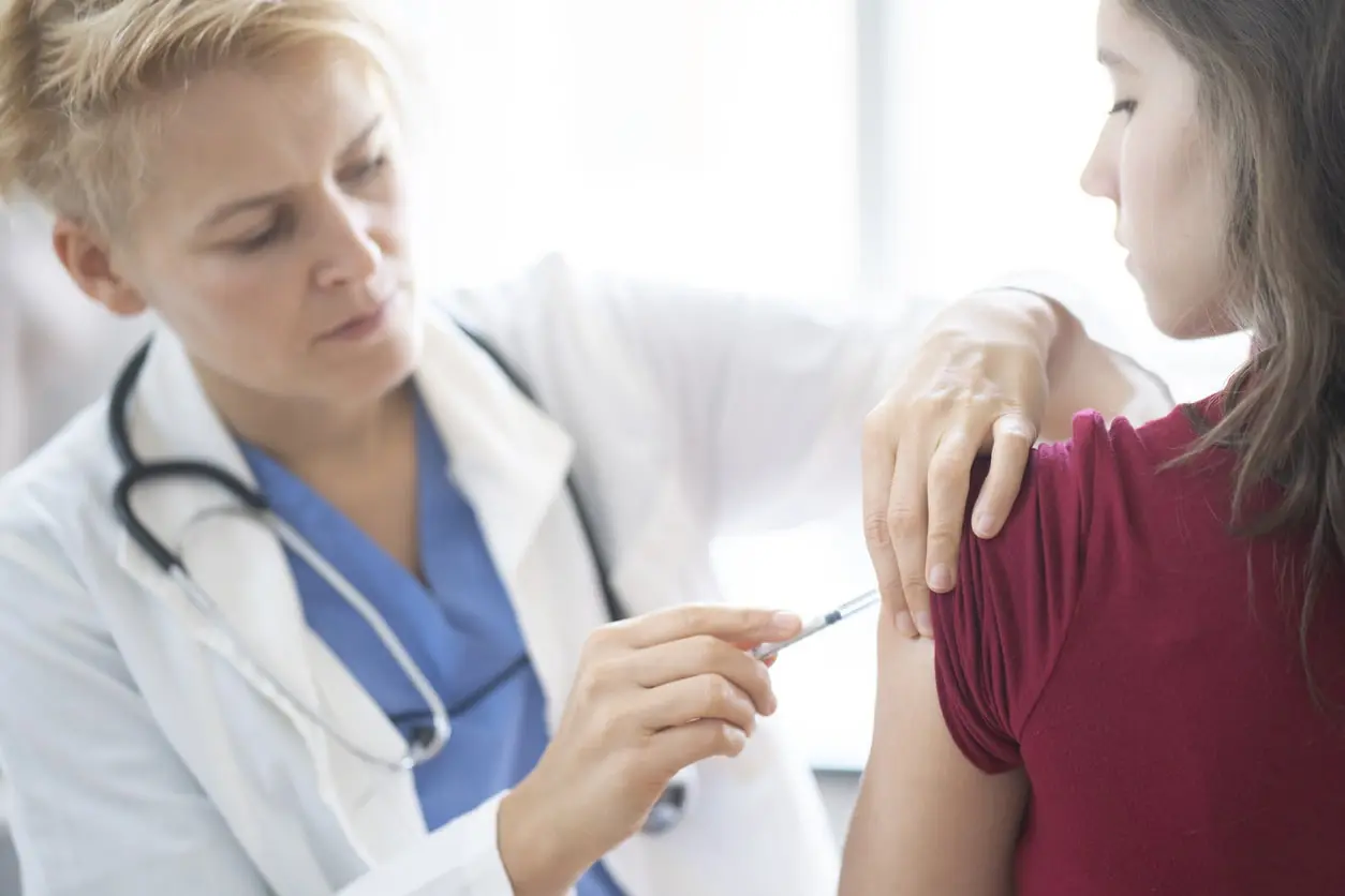 A healthcare professional administers an injection to a patient’s upper arm in a medical setting.