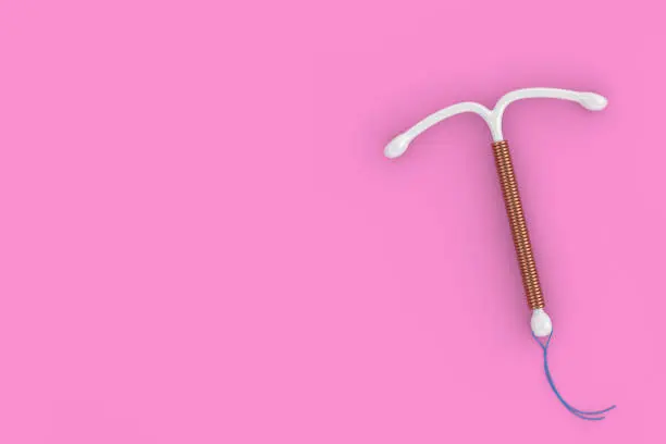 A copper intrauterine device (IUD) is displayed on a pink background.