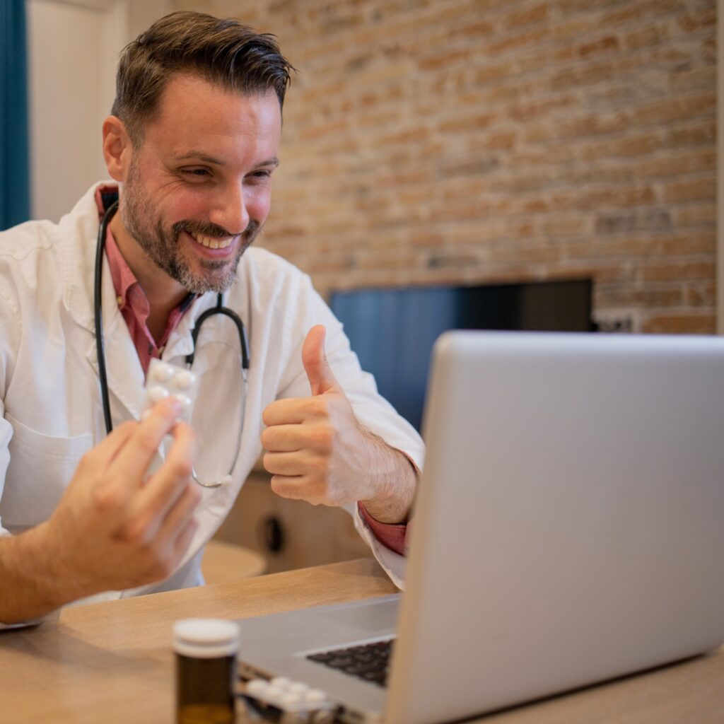 Doctor holding tablets in front of laptop doing online consultation