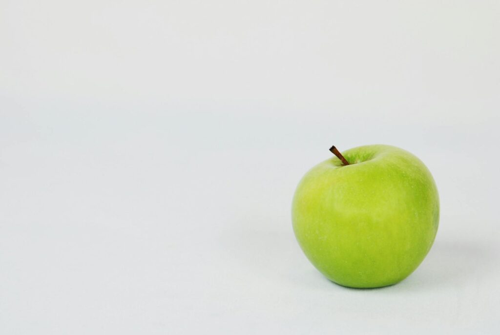 A single green apple resting on a plain white surface with a neutral background.